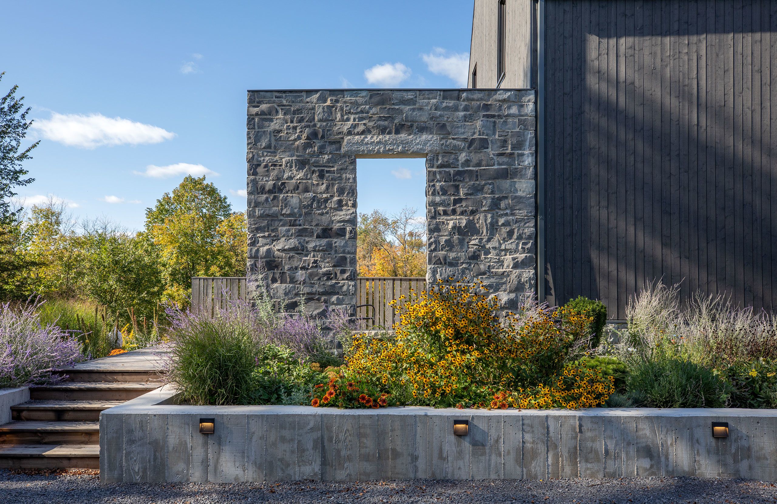 Completed stone Window Wall with garden in front bordered by a textured board-faced cement retaining wall with lighting inserts